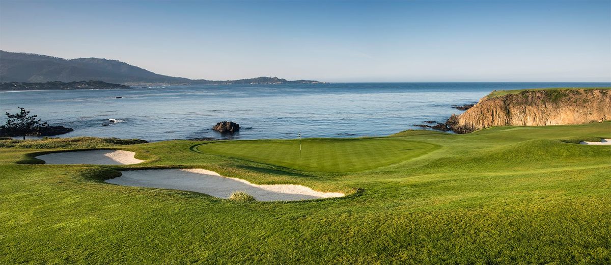 Pebble Beach golf links — the iconic 18th green meeting Carmel Bay at sunset, Lone Cypress in the distance